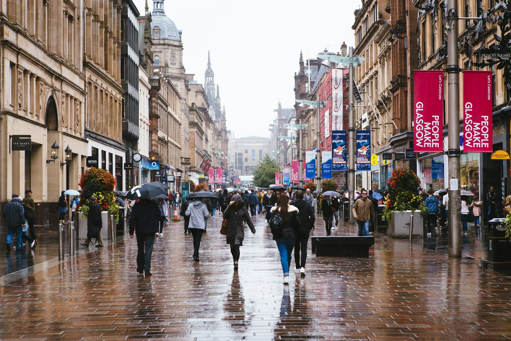 Shoppers with umbrellas on a rainy Buchanan Street in Glasgow, with People Make Glasgow banners overhead