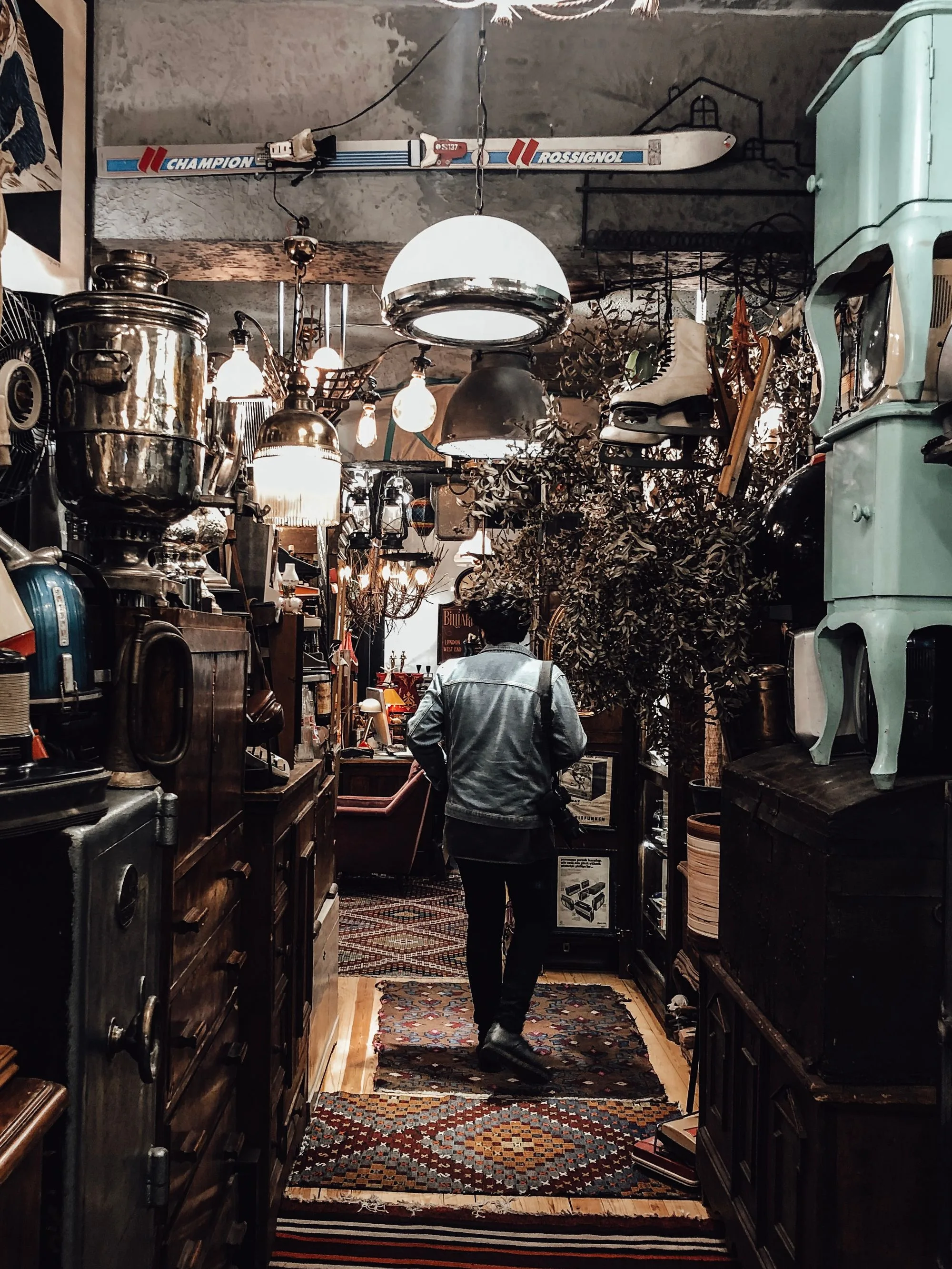 Browsing a densely packed antique shop aisle filled with vintage lamps, furniture and curiosities