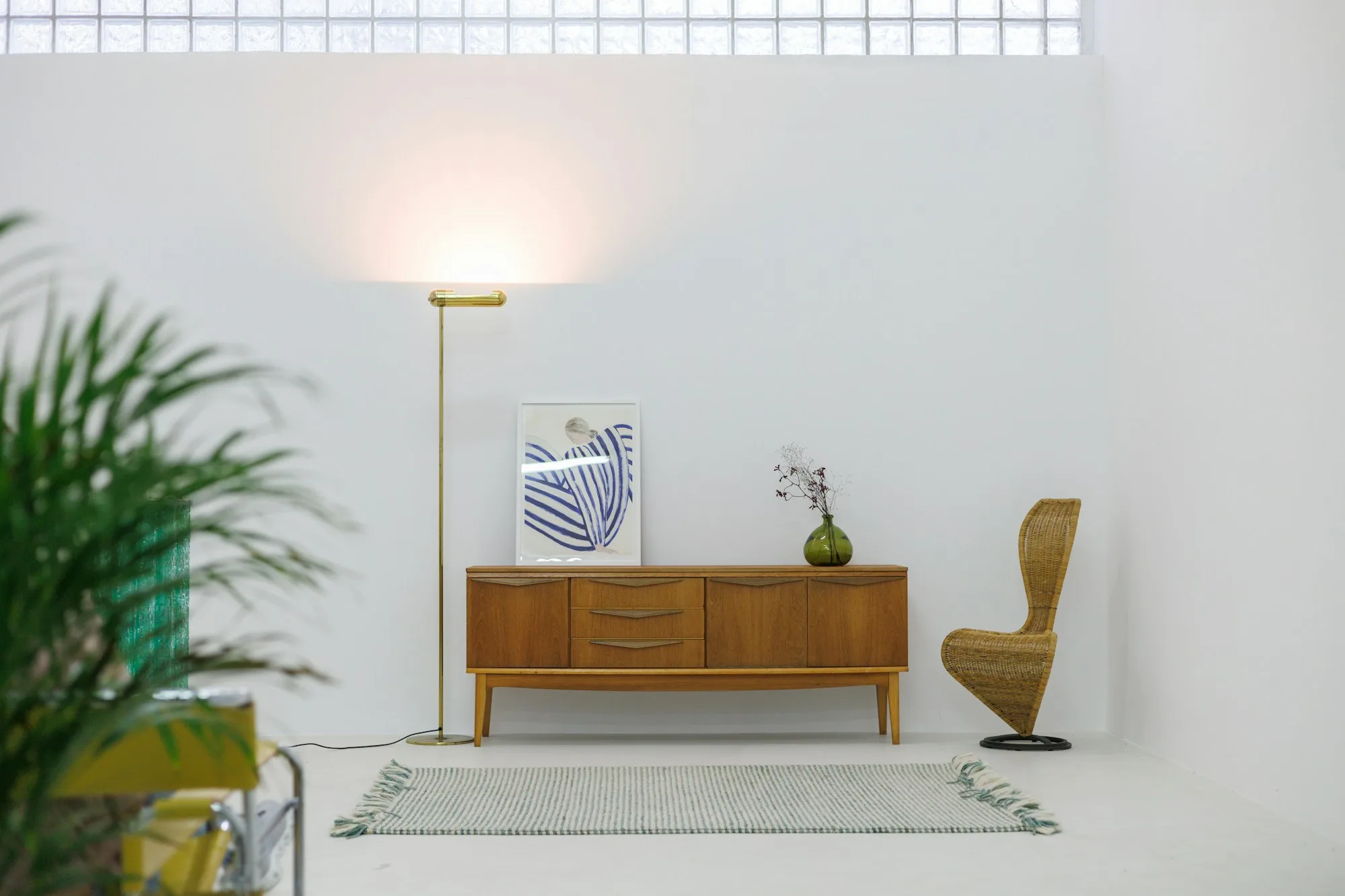 Teak mid-century sideboard with sculpted drawer pulls and tapered legs, styled with a framed print, brass floor lamp and wicker chair